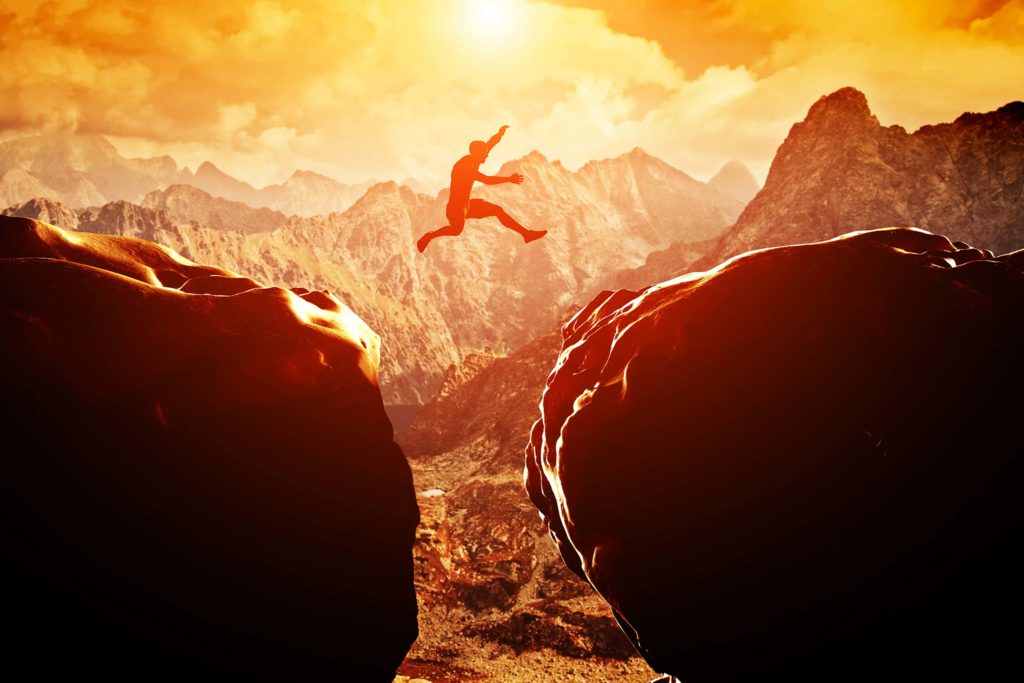 Mountain climber jumping a vast span between boulders